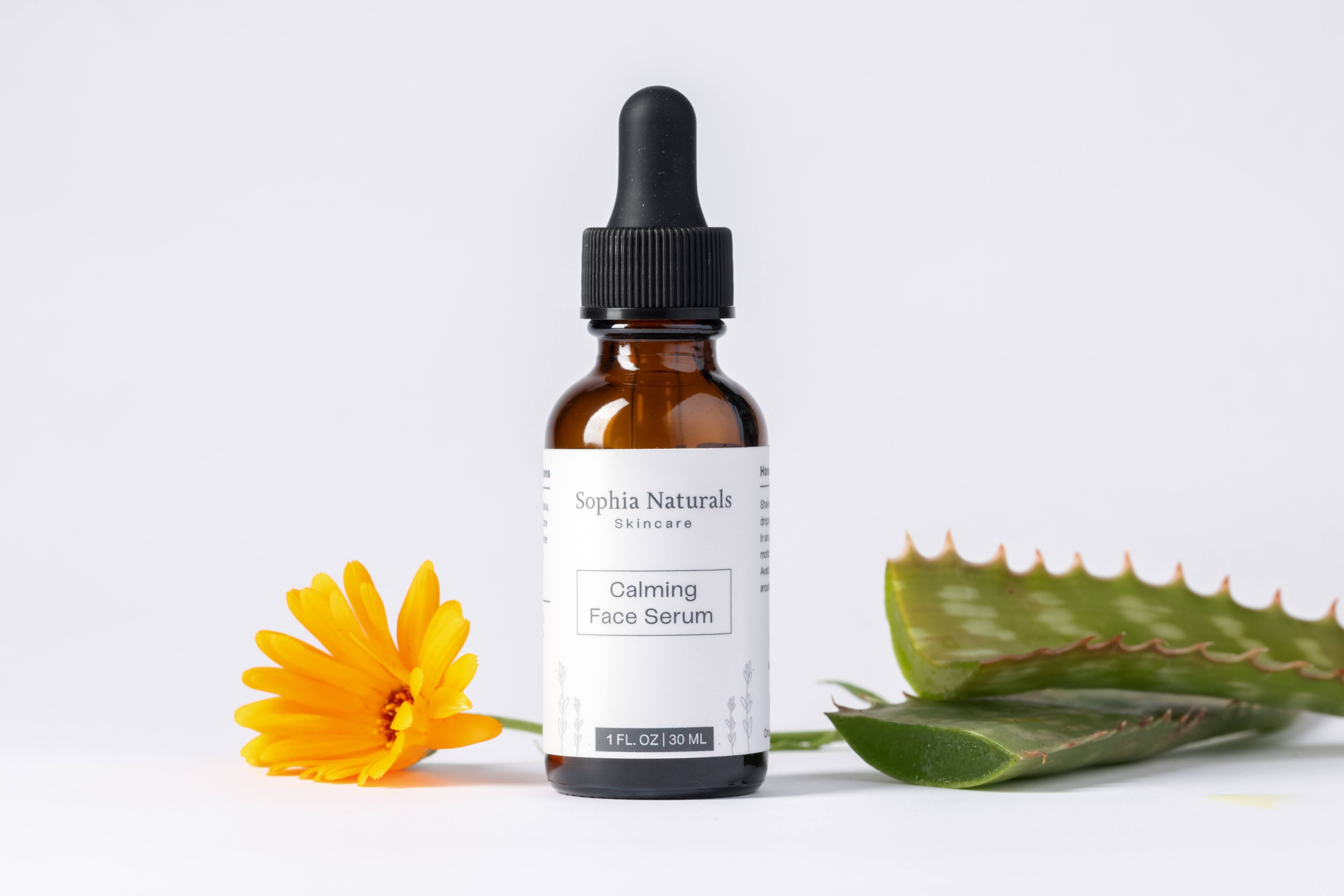 Brown glass bottle of face serum with a black dropper, next to a yellow daisy and an aloe vera leaf. Organic Skincare.
