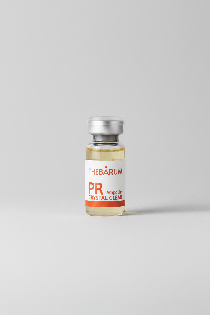 A small clear glass ampoule vial with a silver metal cap and a white label reading 'THEBÁRUM PR Ampoule CRYSTAL CLEAR' in orange text, shown on a plain white background.