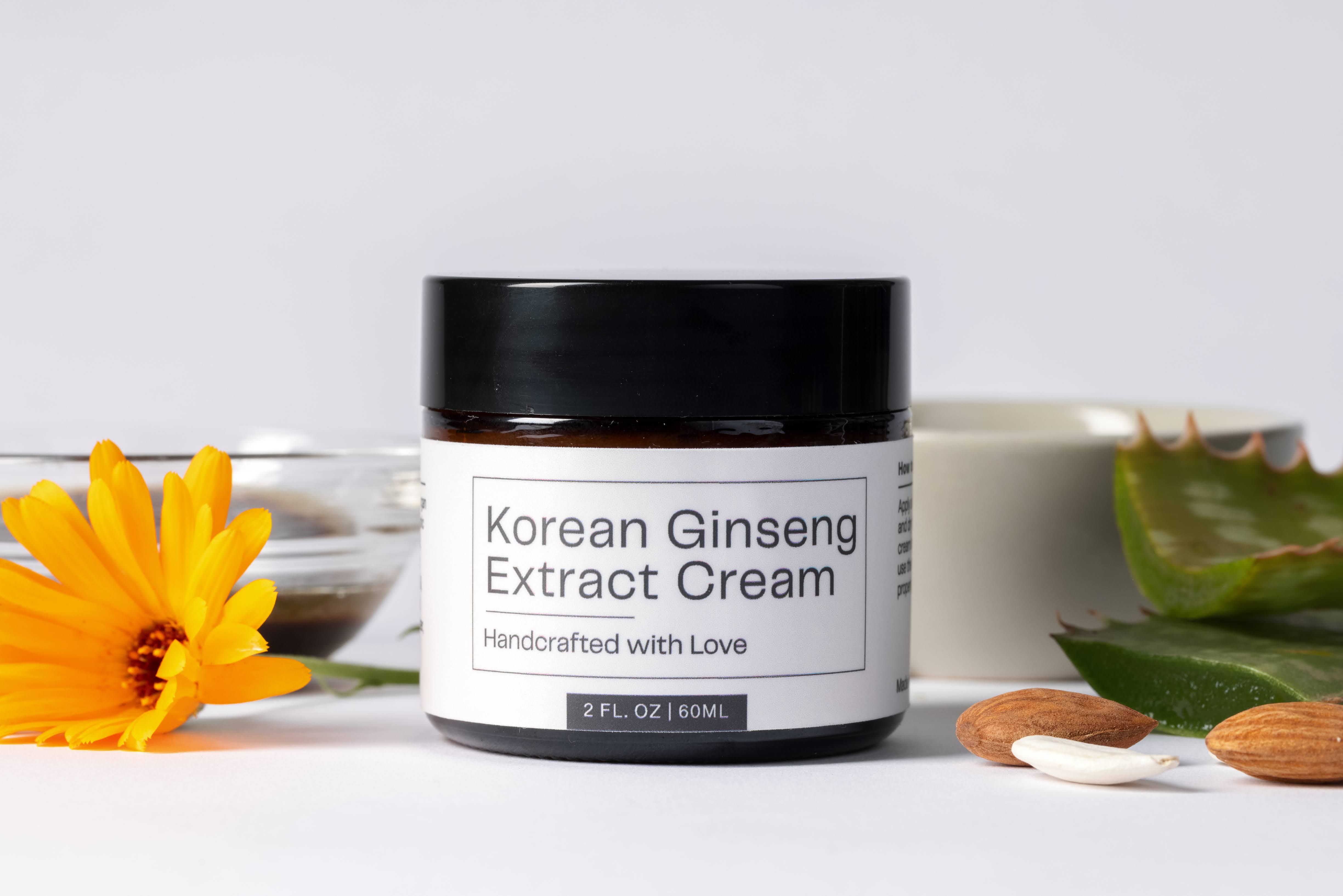 Korean Ginseng Extract Cream in a 2 oz jar, handcrafted skincare product displayed with natural ingredients like aloe vera, almonds, and a yellow flower on a clean white background.